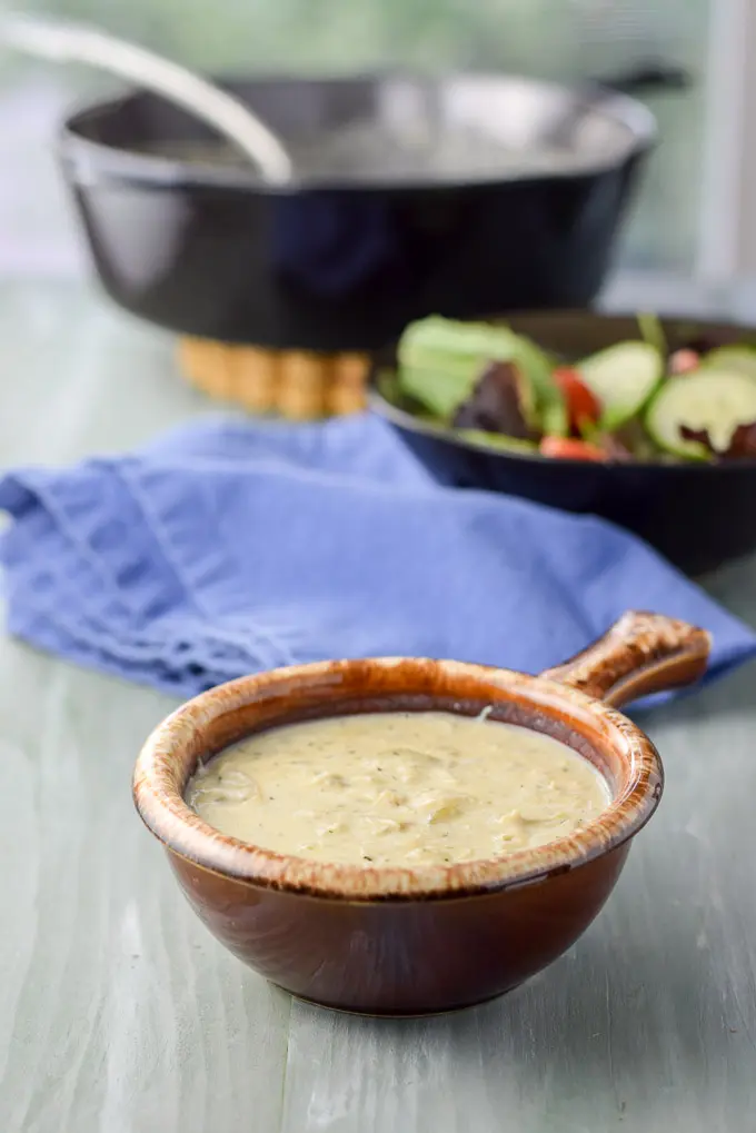 Different view of the bisque in a brown crock with a napkin, salad and pan in the background