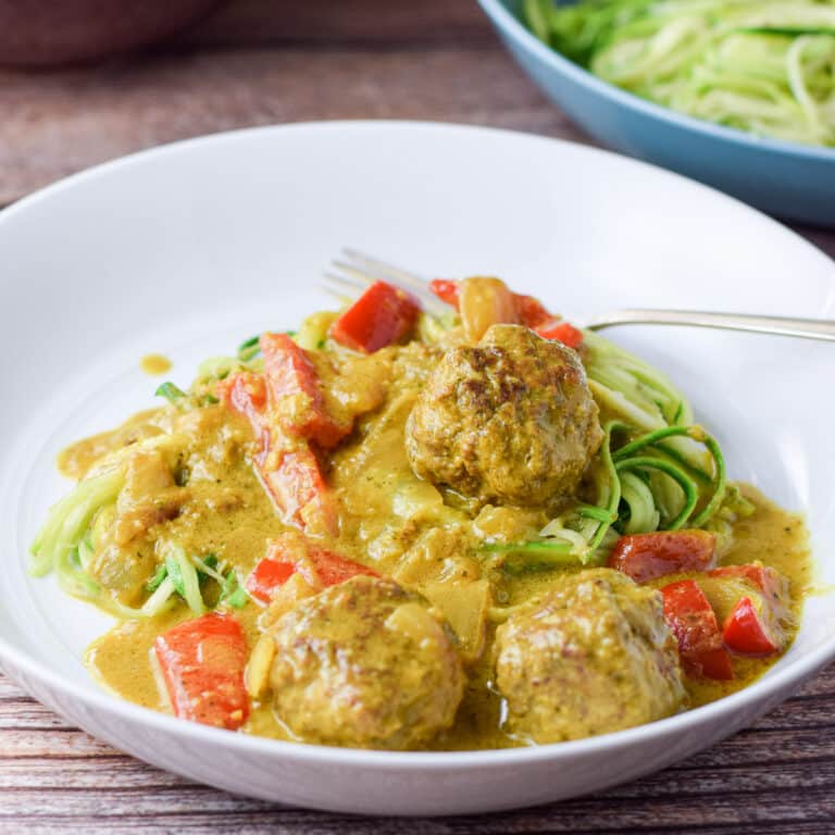 A white plate with meatballs in a curry sauce on zoodles - square