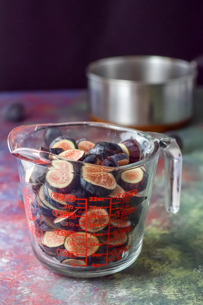 Cut up figs in a glass measuring cup with a pan in the background