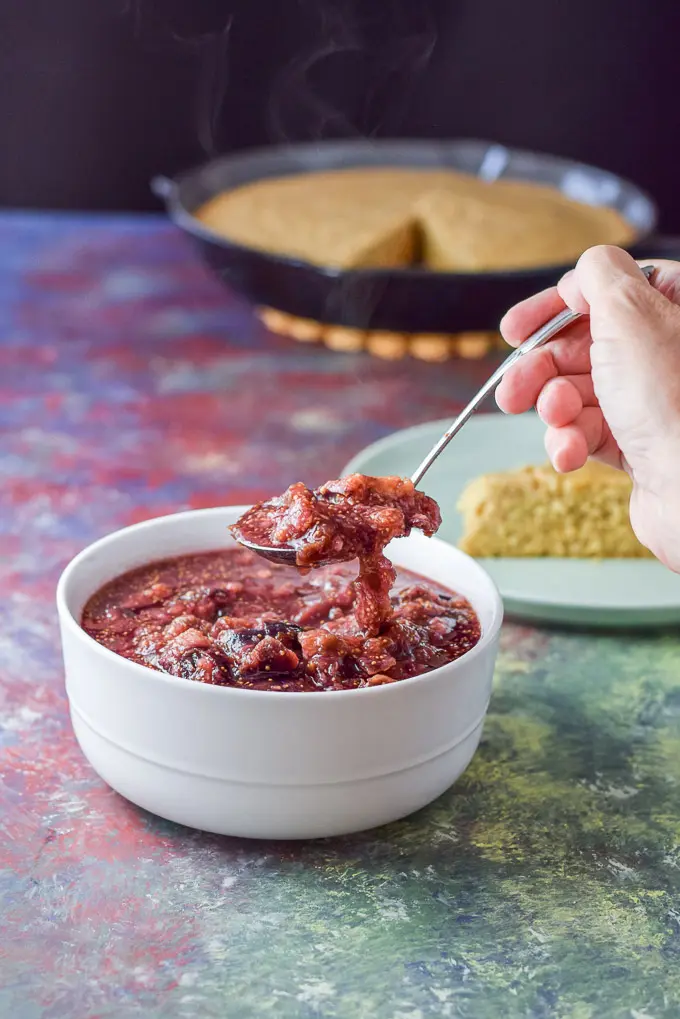 A spoonful of the fig sauce held over a white bowl with some cornbread in the background