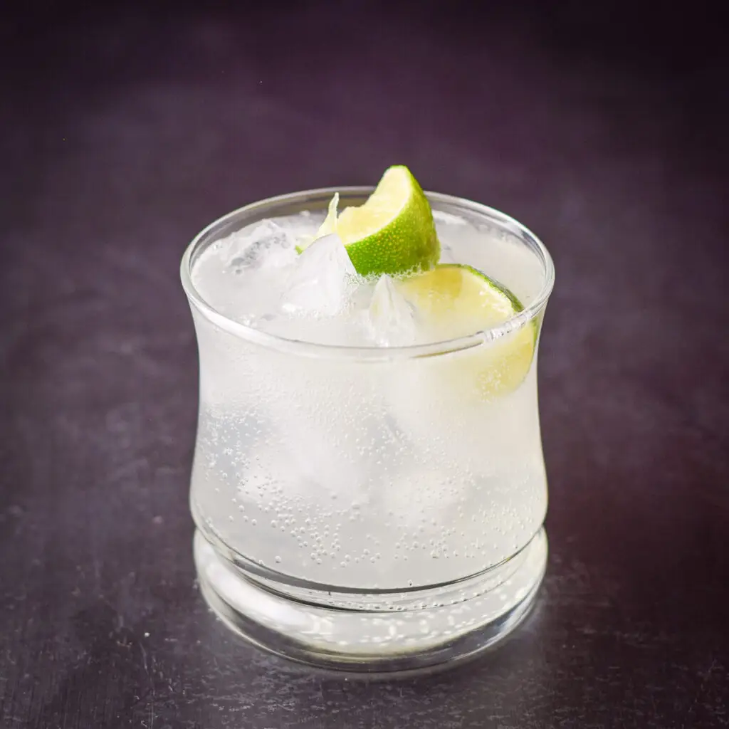 A close view of the cocktail and two lime wedges in a double old fashioned glass - square