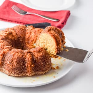 A cake server with a piece of cake on it held over the rest of the cake - square