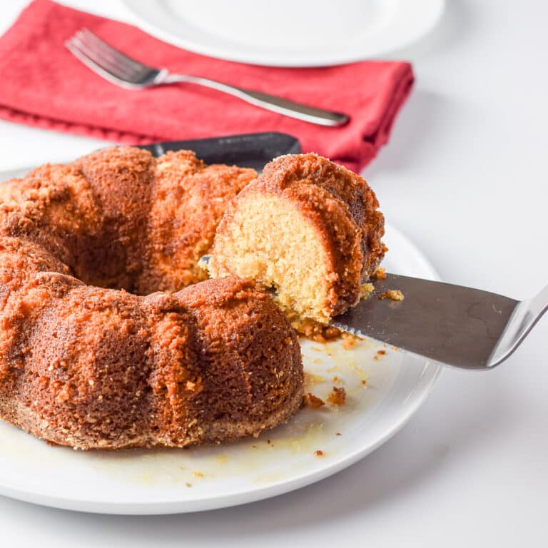 A cake server with a piece of cake on it held over the rest of the cake - square
