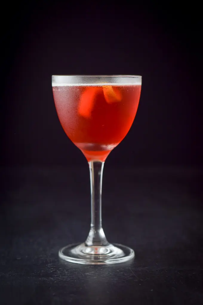 Vertical view of the red cocktail with a lemon twist on a black background