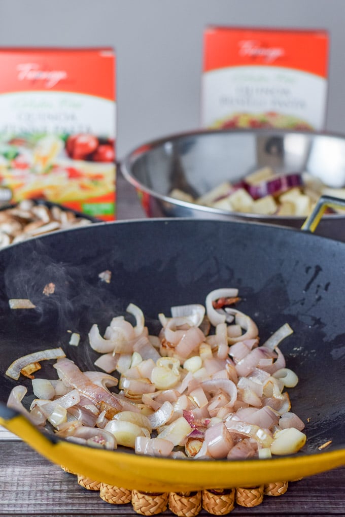 Shallots saut&eacute;ed in a wok and cut up eggplant in the background