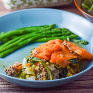 Close up of a blue bowl with the shepherds pie and asparagus in it - square