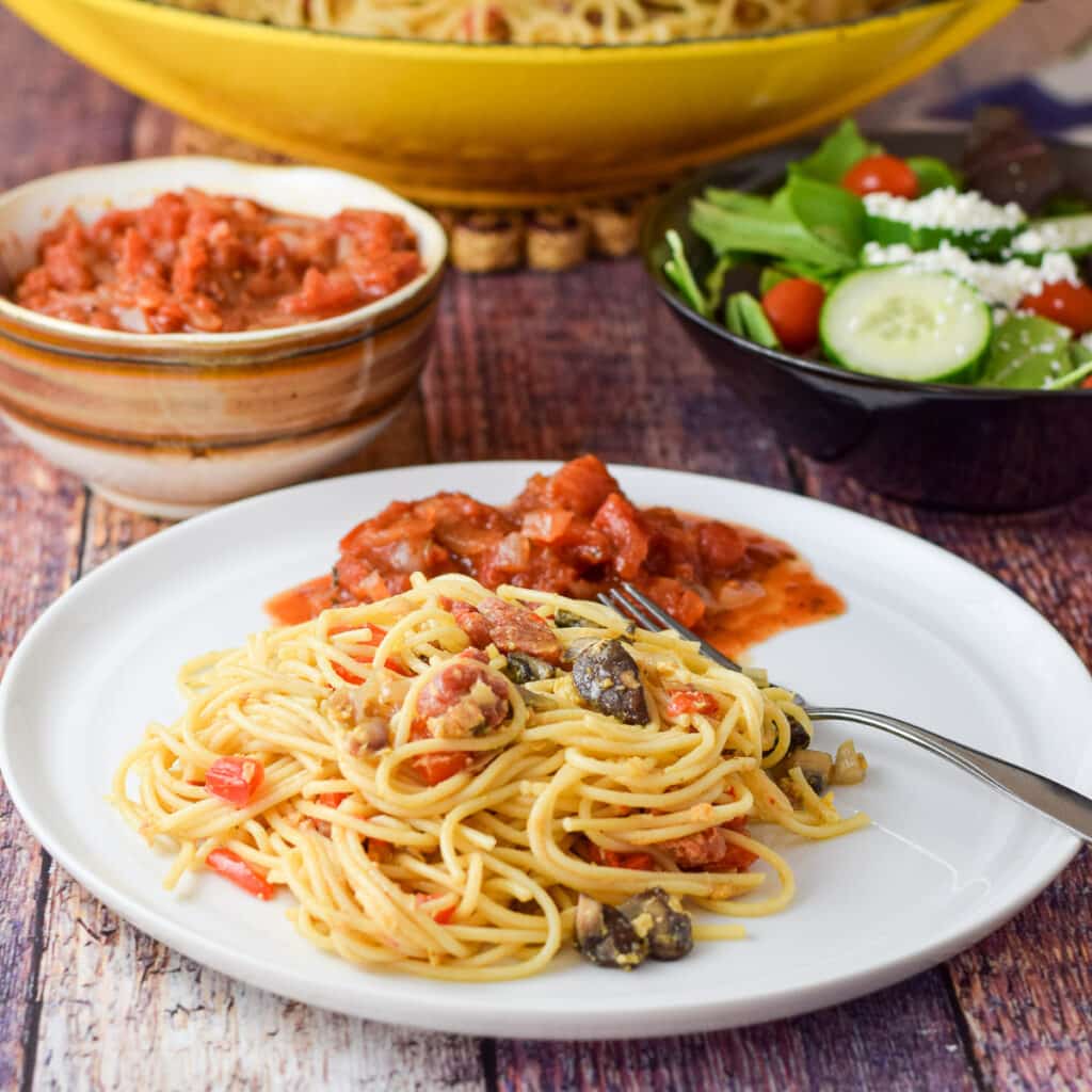A white plate with spaghetti egg on it with some chunky sauce behind it - square