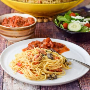 A white plate with spaghetti egg on it with some chunky sauce behind it - square