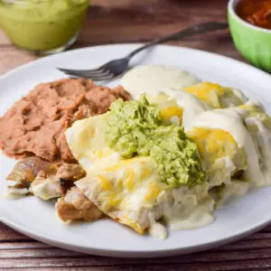 Guacamole and more sour cream sauce draped over the enchiladas with beans on the plate as well