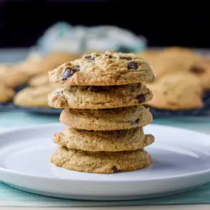 Five cookies stacked on top of each other on a white plate with cookies on a rack in the background - square