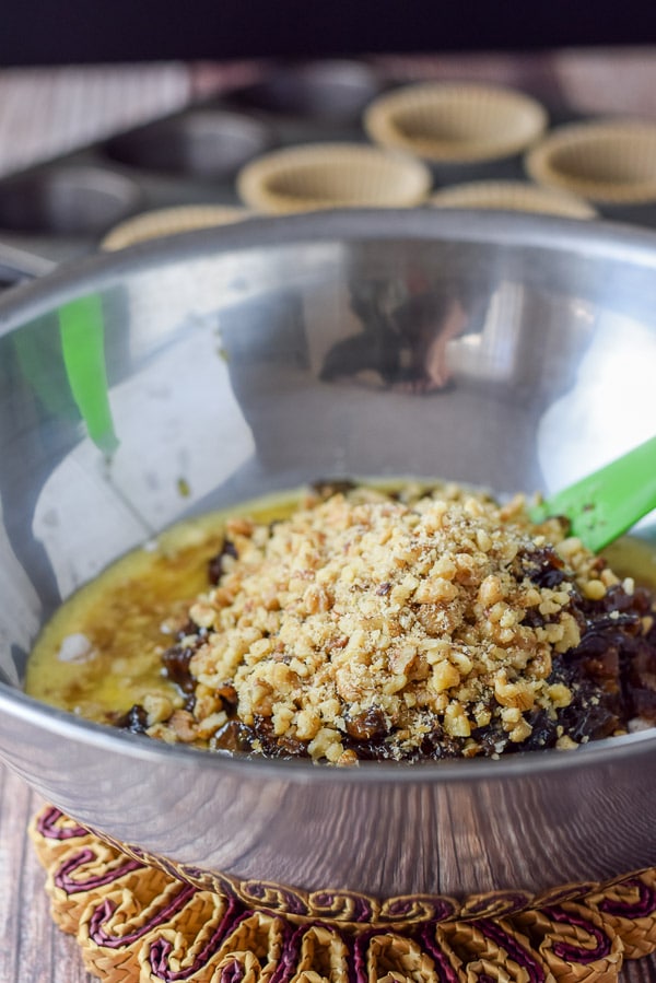A big bowl with all the ingredients in it with the nuts on top. There is a muffin tin in the back