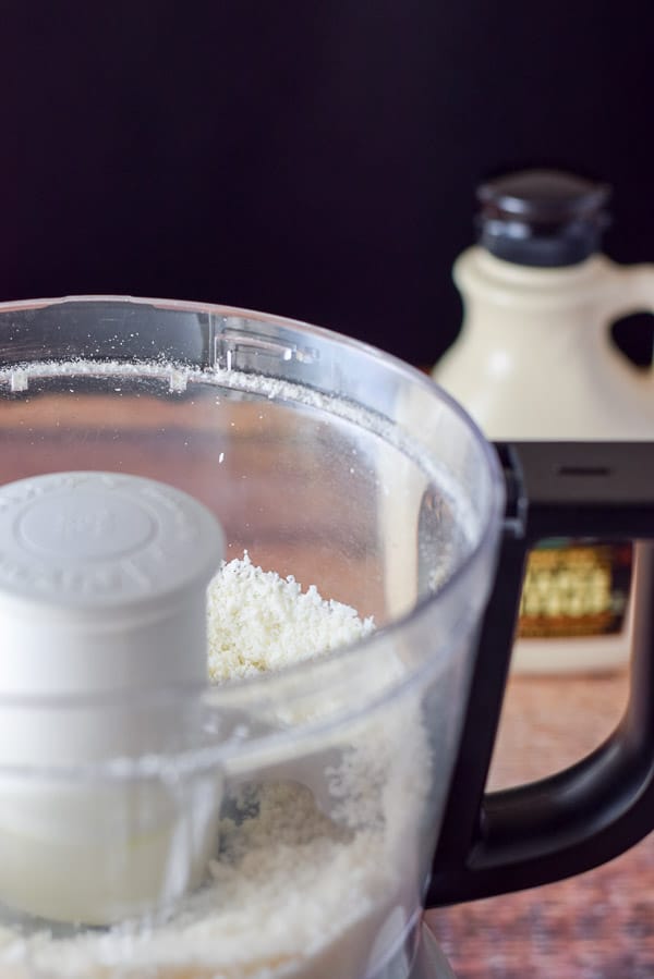 Closeup of the food processor container with shredded coconut, coconut flour and salt mixed together.
