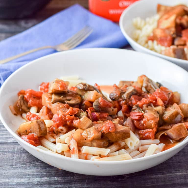A deep white bowl filled with penne with veggies on it - square