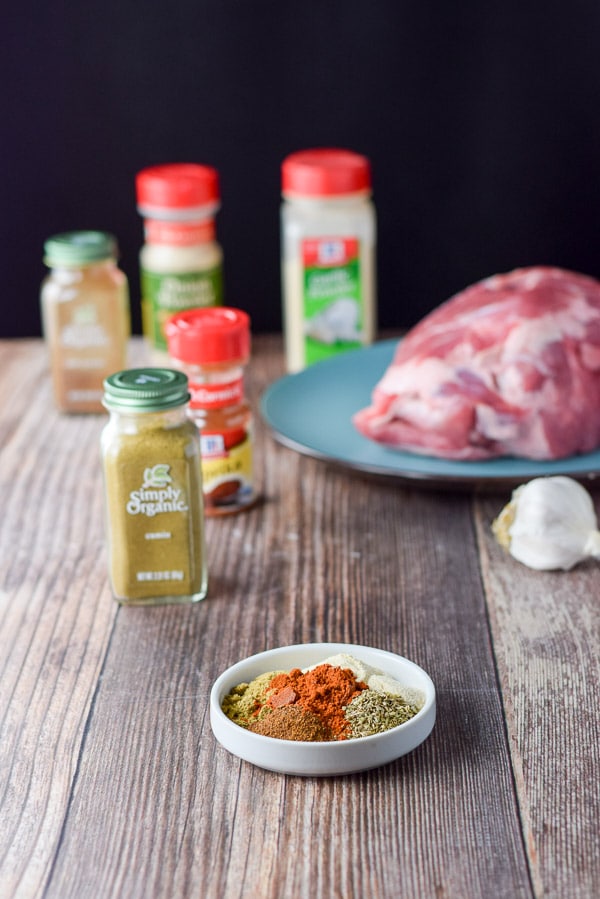 Spices measured in a white dish along with the bottles, raw pork and garlic in the background