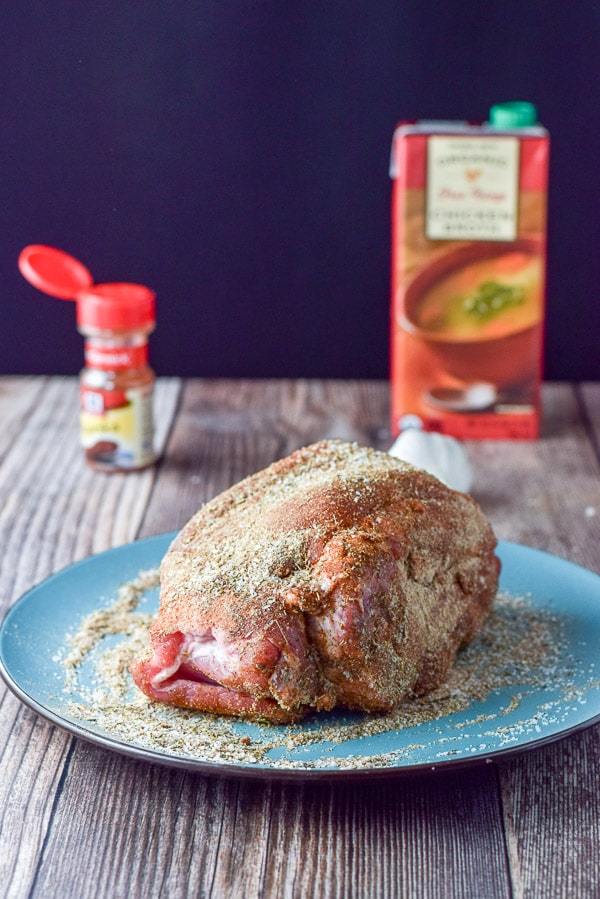 All the spices for the rub patted on the pork shoulder with broth and paprika in the background