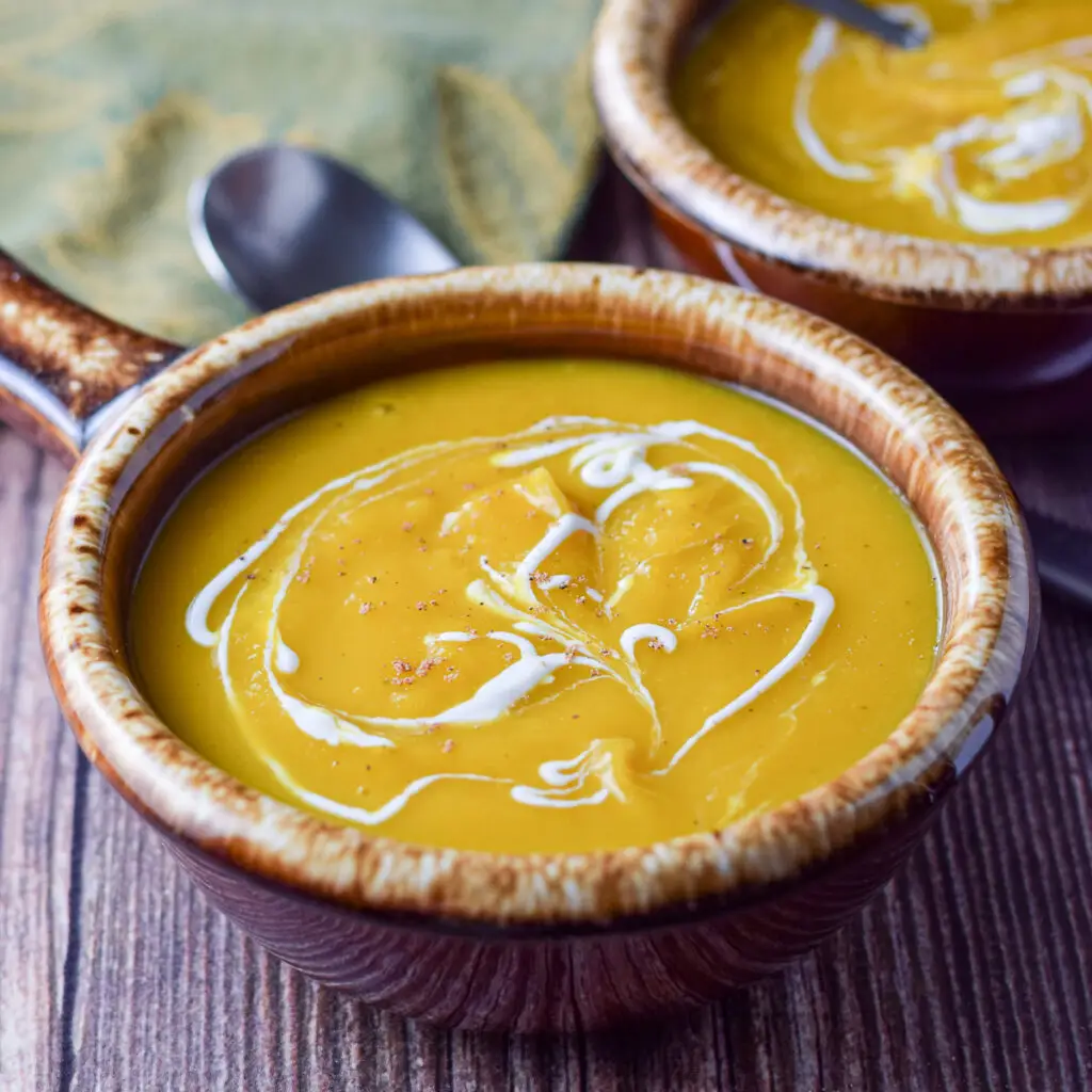 Two brown crocks filled with squash soup with sour cream squiggled on top - square