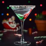Vertical view of the martini with lights, santa claus in a sled and candy canes on the table - square