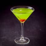 A maraschino cherry dropped into the green midori cocktail - square