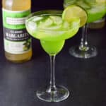 A classic margarita glass filled with the melon margarita with a lime wheel on the rim of the glass