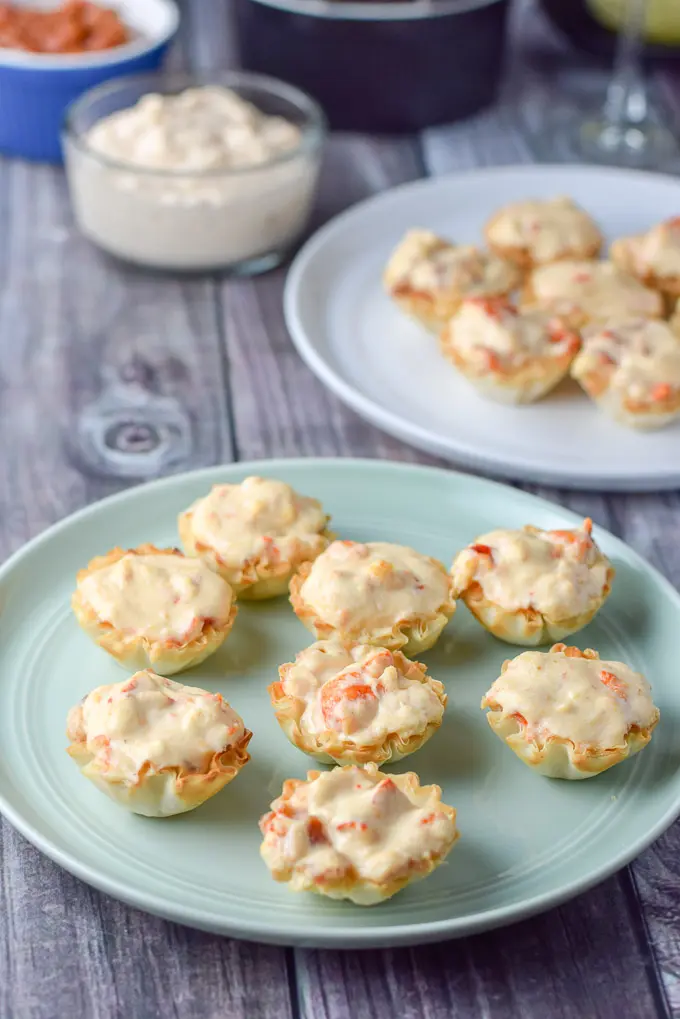 Close up of the green plate of lobster filled phyllo cups with extra cream cheese lobster in the background