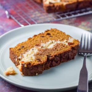 A green plate with a piece of pumpkin bread on it with a wire rack in the background - square