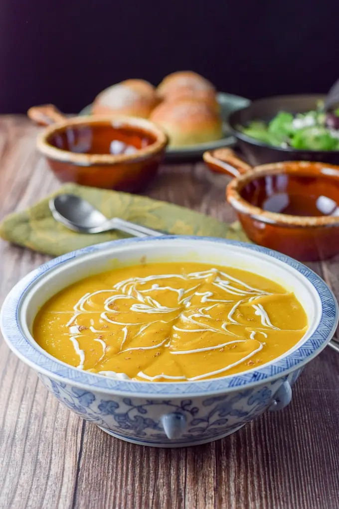 Sour cream squiggled on the thick squash soup with crocks and rolls in the background