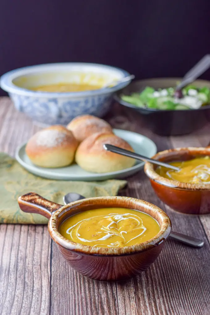 two bowls of squash soup with rolls in the background
