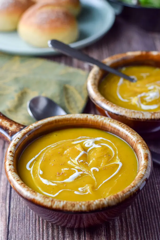 Two brown crocks filled with squash soup with sour cream squiggled on top