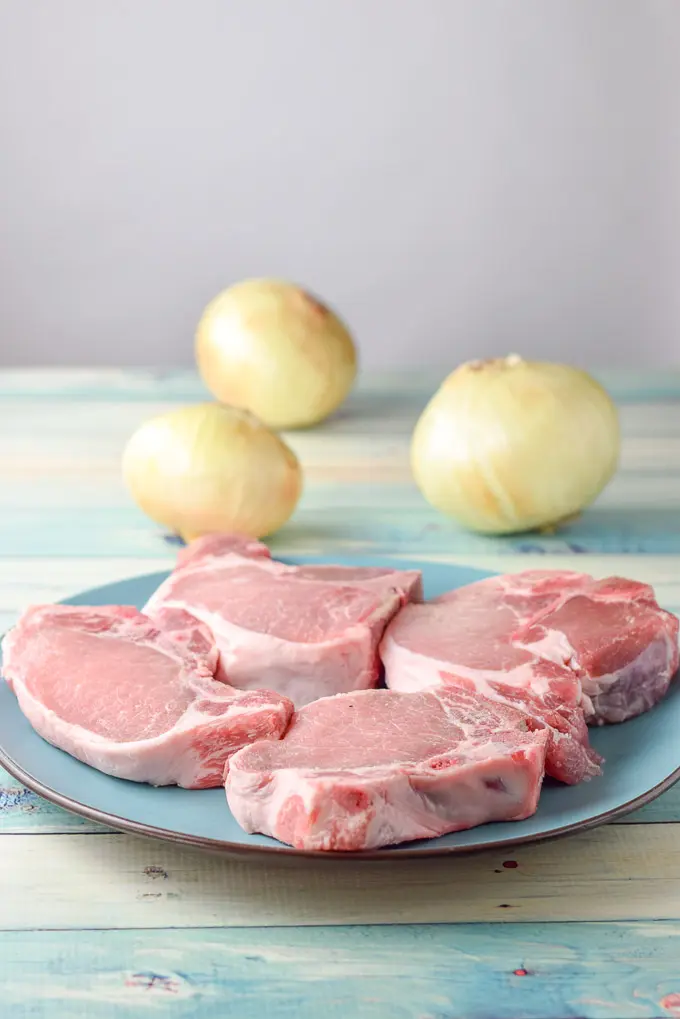Four pork chops on a plate with some onions in the background
