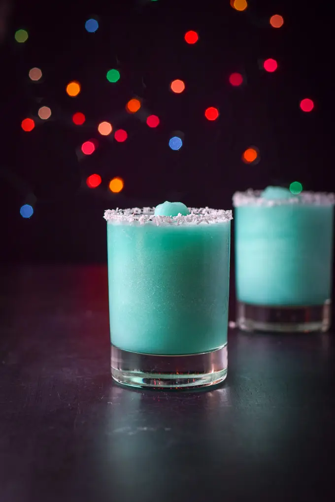 Vertical view of the frozen blue cocktails with coconut rims and lights in the background