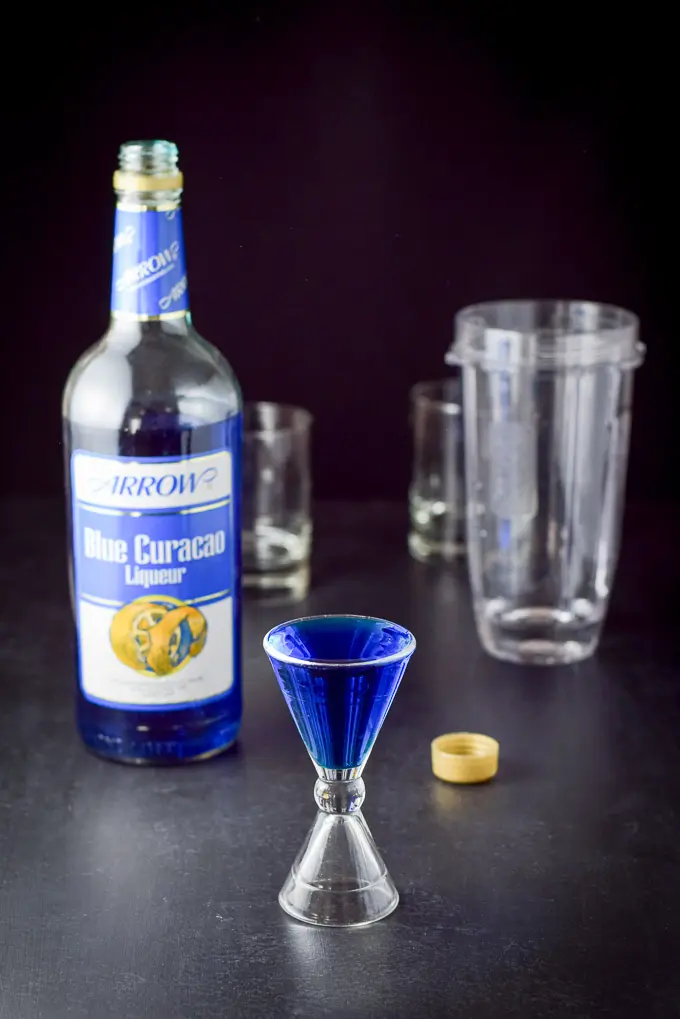 Blue Curacao poured out with the bottle, blender and glassware in the background