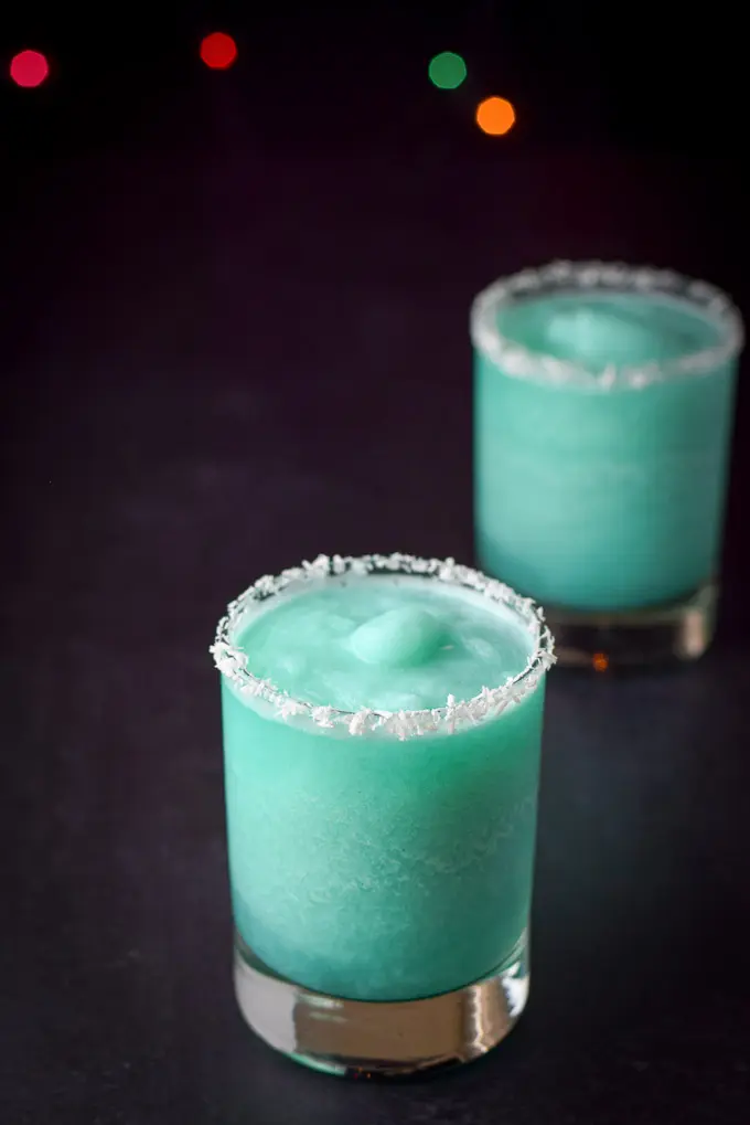 Close up of the blue cocktail in two coconut rimmed glasses on a black table with some lights in the background