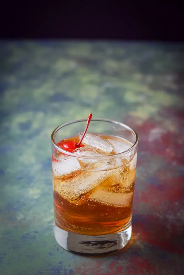 Close up of the ice filled double old fashioned glass with the Manhattan and a cherry