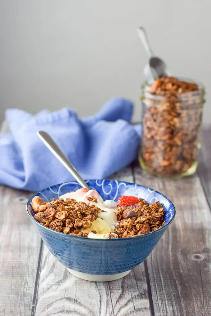 A blue bowl filled with fruit, yogurt and granola with a jar of granola in the background