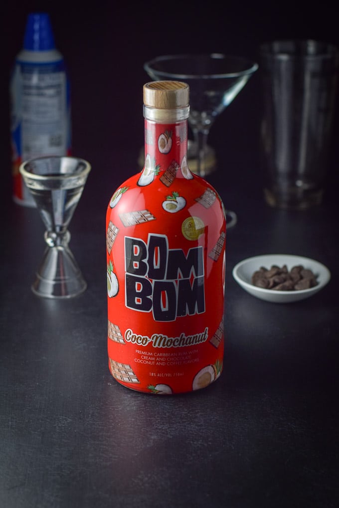Bom Bom liqueur and vanilla vodka on a table with chocolate chips, shaker, glass and whipped cream