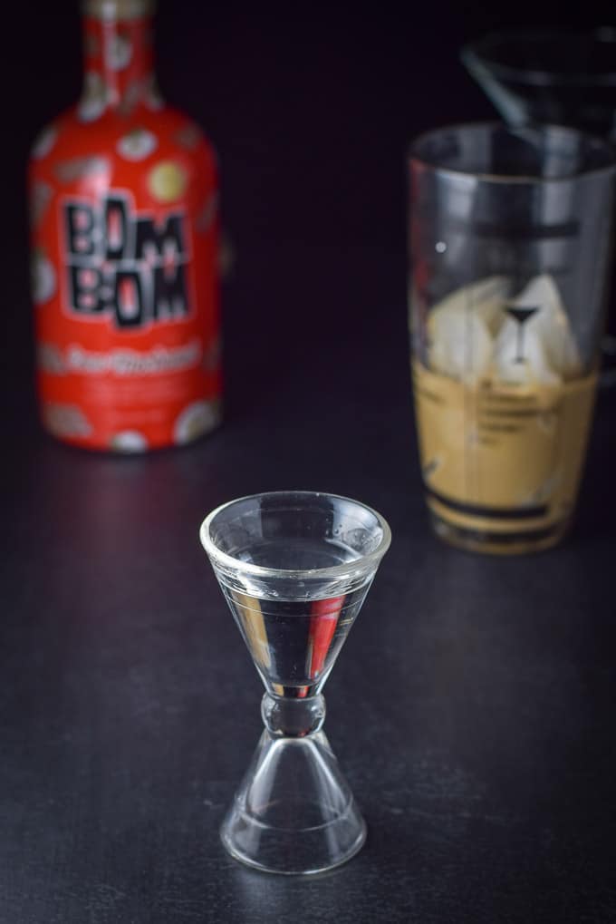 The vanilla vodka in the measuring glass with the bottle and shaker in the background