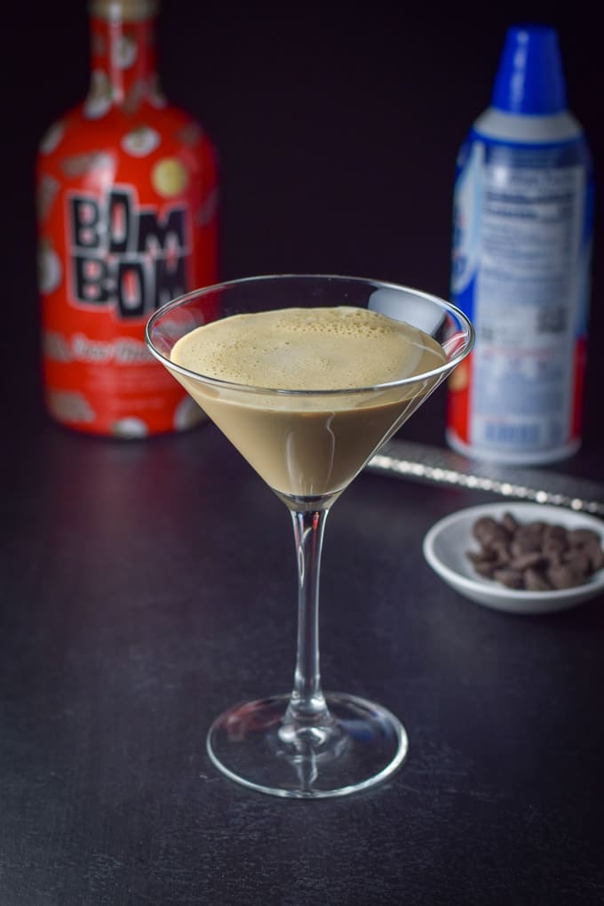The chocolate cocktail shaken and poured into the glass with some chocolate chips and whipped cream in the background