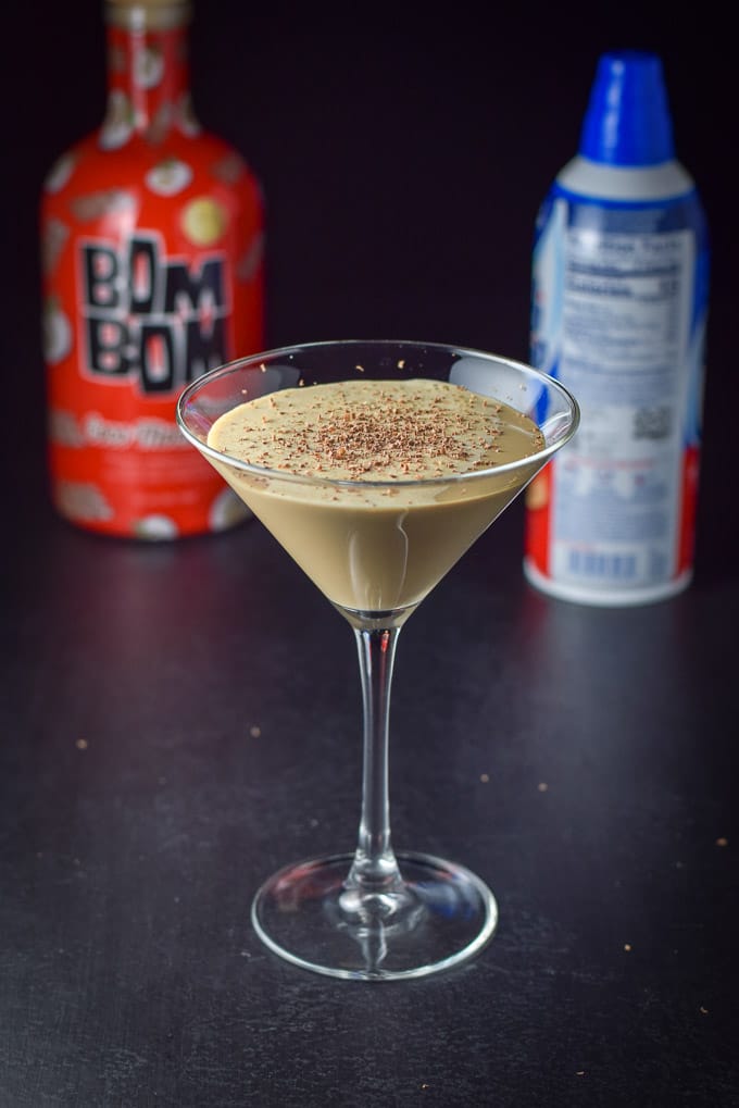 Chocolate chips shaved into the cocktail with the bottle and whipped cream in the background