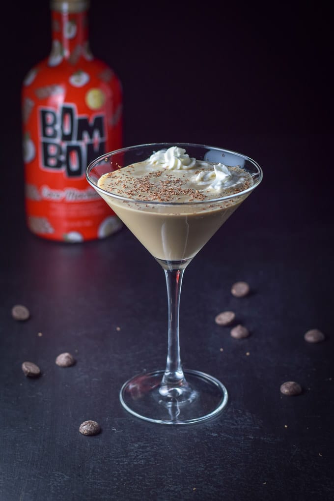 2 dollops of whipped cream in the cocktail which chocolate chips in the background and the bottle