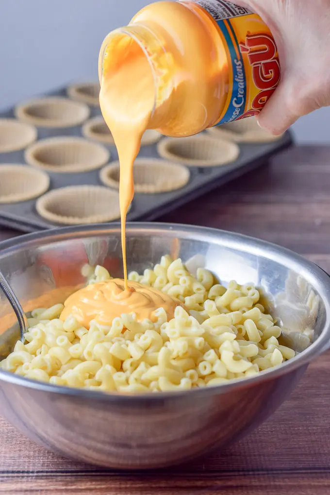 A hand pouring cheese sauce in the cooked elbow macaroni