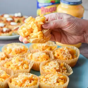A hand holding a mac and cheese in a muffin cup with a bite taken out of it