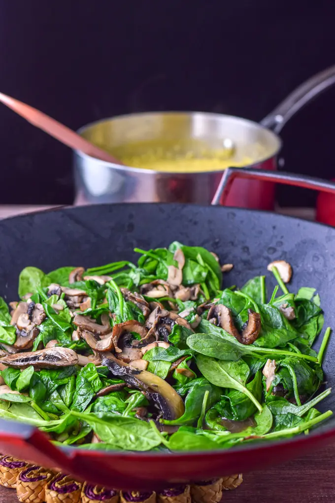 Mushrooms and spinach cooked in a wok with a pan of polenta in the background