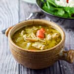 A crock of chicken soup with a salad in the background - square