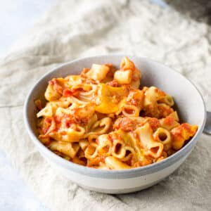 A grey bowl of bacon tomato pasta on a beige napkin - square
