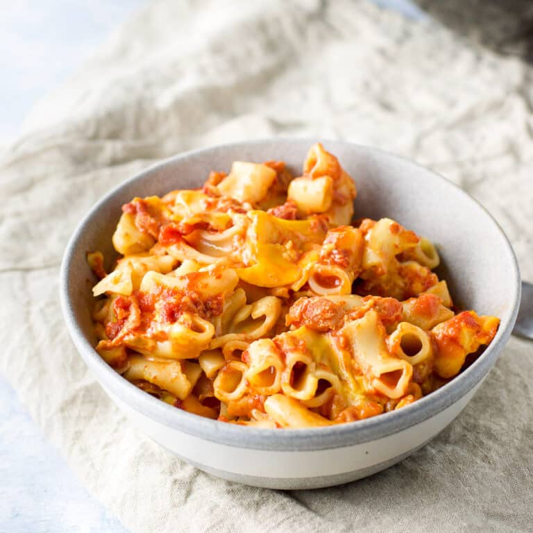 A grey bowl of bacon tomato pasta on a beige napkin - square