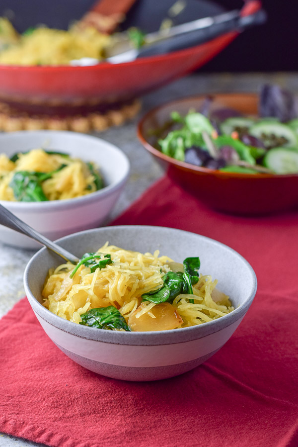 Grey bowls with spaghetti squash in it with a salad and the wok in the background