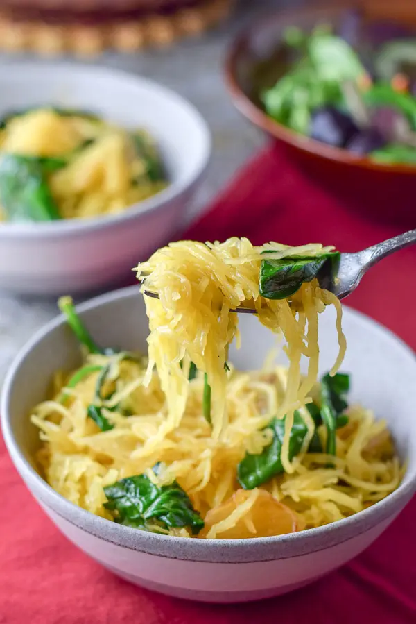 A forkful of spaghetti squash with sauce and spinach over the grey bowl