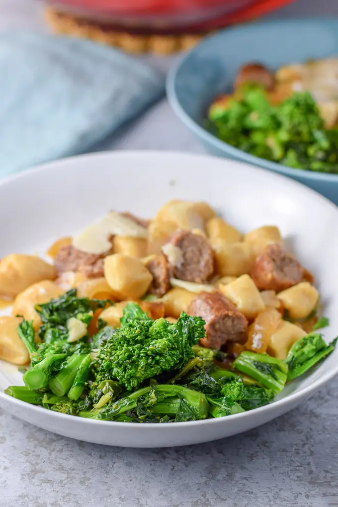 A close up view of the broccoli in a plate with some sausage and gnocchi