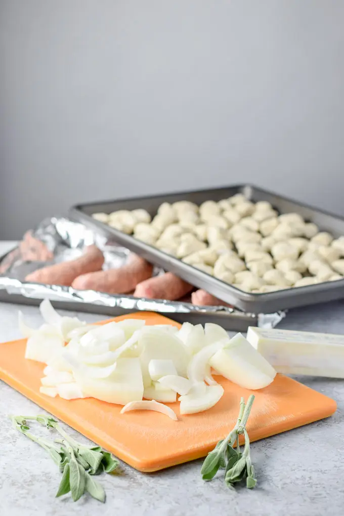 Sliced onion, butter, sage, sausages and gnocchi on a table