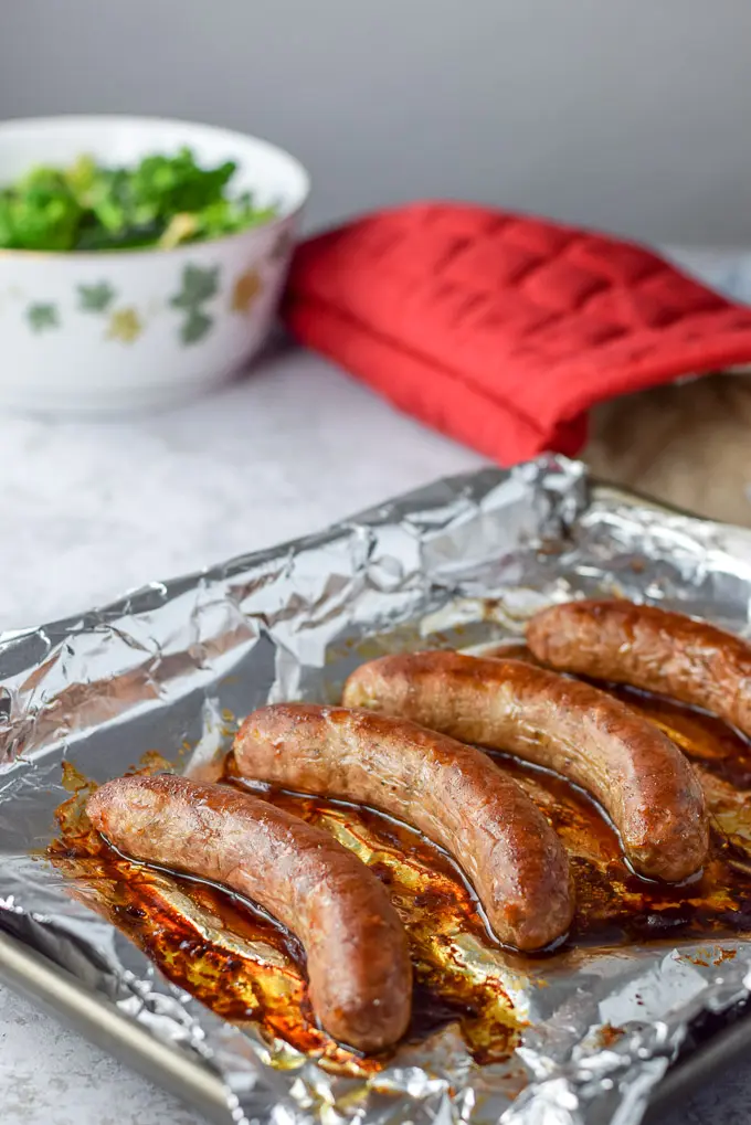Sausage baked on a tray with cooked broccoli in the background